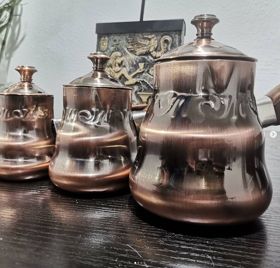 cafetera con tapa, de acero inoxidable color cobre, mango de madera y letras árabe.